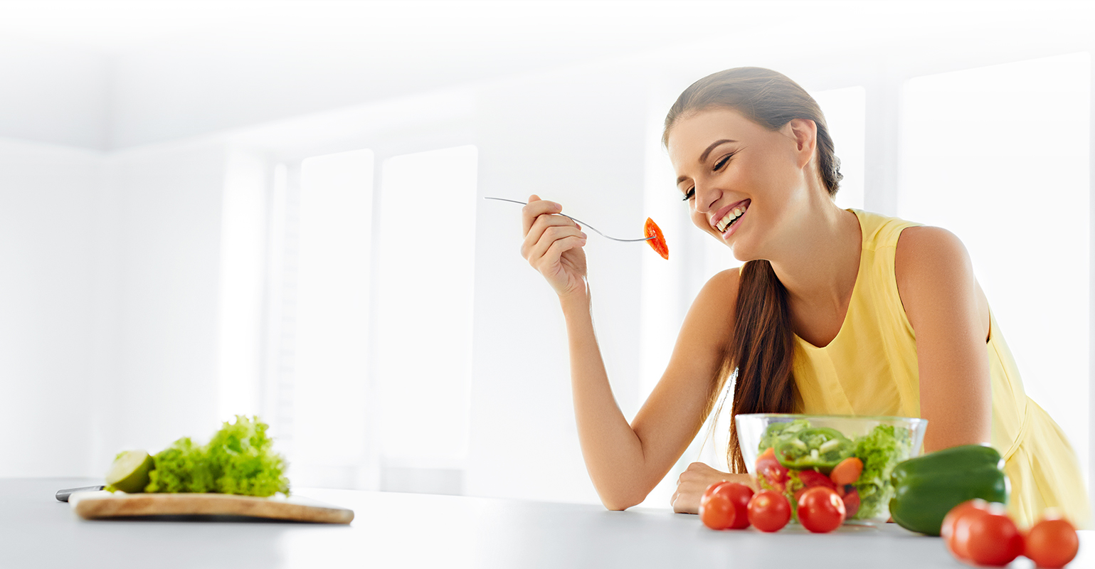 Kobieta siedzi i je posiłek zaplanowany przez dietetyk Kalisz Uniejewscy, złożony z warzyw. Jest szczupła, uśmiechnięta i ładna.