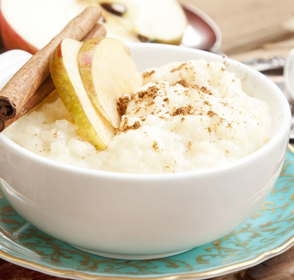 Rice Pudding with Apple Slices and Cinnamon Spice Sticks on Wooden Background